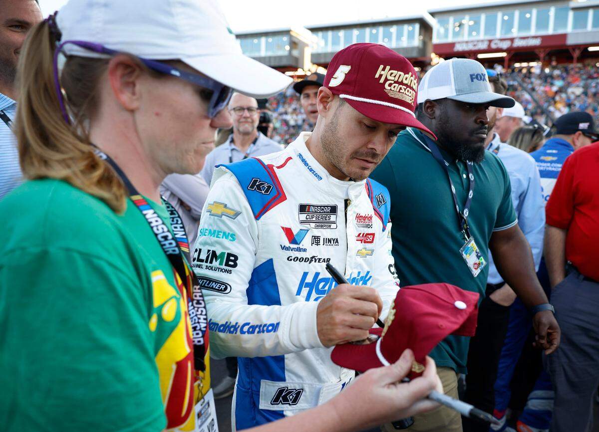 NASCAR Cup Series driver Kyle Larson, right, signs an autograph for a fan as he walks to his car at North Wilkesboro Speedway in North Wilkesboro, NC prior to the running of the NASCAR All-Star Race. Larson had earlier qualified fifth for the Indianapolis 500 on Sunday, May 19, 2024.