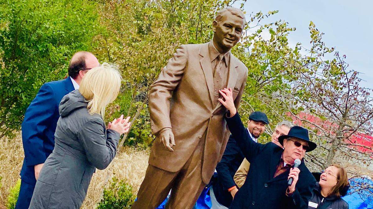 Shown at the unveiling of Phil Van Every’s bronze sculpture on the Trail of History near uptown Charlotte on Saturday, Nov. 16, 2019, are, from left, T. Glenn, Van Every’s grandson in blue suit; Quincy Foil White, Van Every’s granddaughter; Tony Zeiss, chairman of the Trail of History’s board of directors shown with microphone as he addresses attendees; sculptor Chas Fagan, directly behind Zeiss; and project manager Tyrone Harmon, wearing hat behind Zeiss.