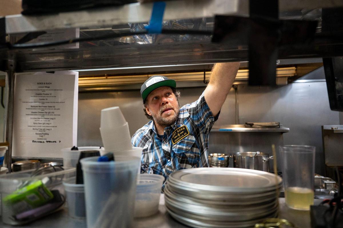 Chef Dano Holcomb reaches for a to-go box while filling an order at the Root Down Kitchen inside Terra Nova Beer Co. in Swannanoa, N.C., Friday, June 27, 2025. Root Down Kitchen was formerly a food truck at The Salvage Station in Asheville before Hurricane Helene destroyed it, prompting Holcomb and his kitchen to relocate to Terra Nova Beer Co. for their current collaboration.