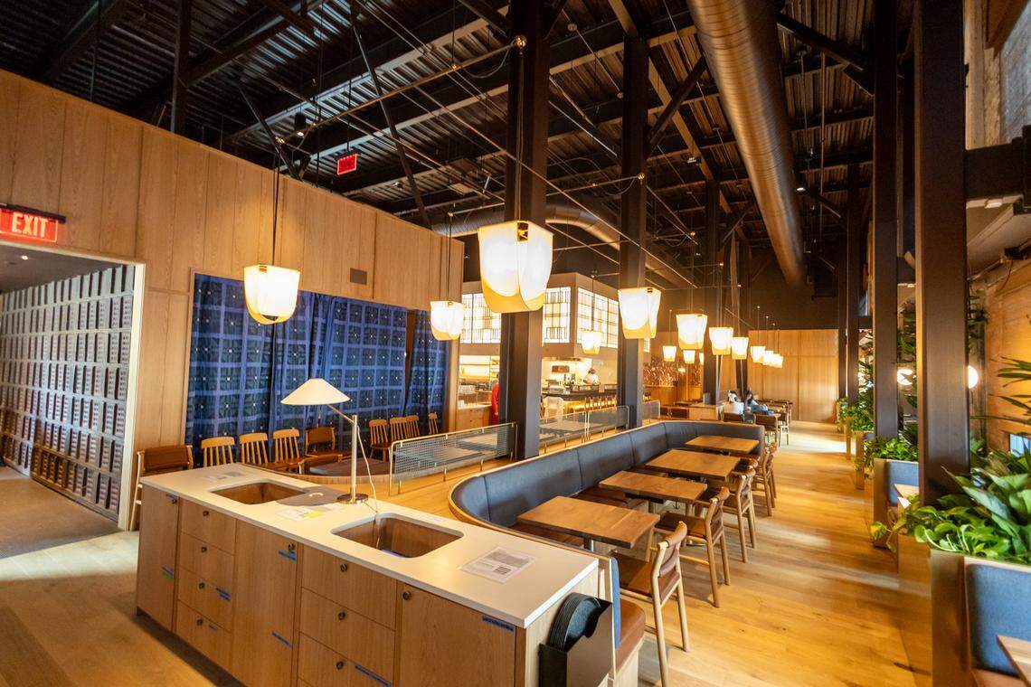 An interior shot looking down the center of the restaurant, showing mirrored seating arrangements with wooden tables and dark grey banquettes separated by a central wooden divider.