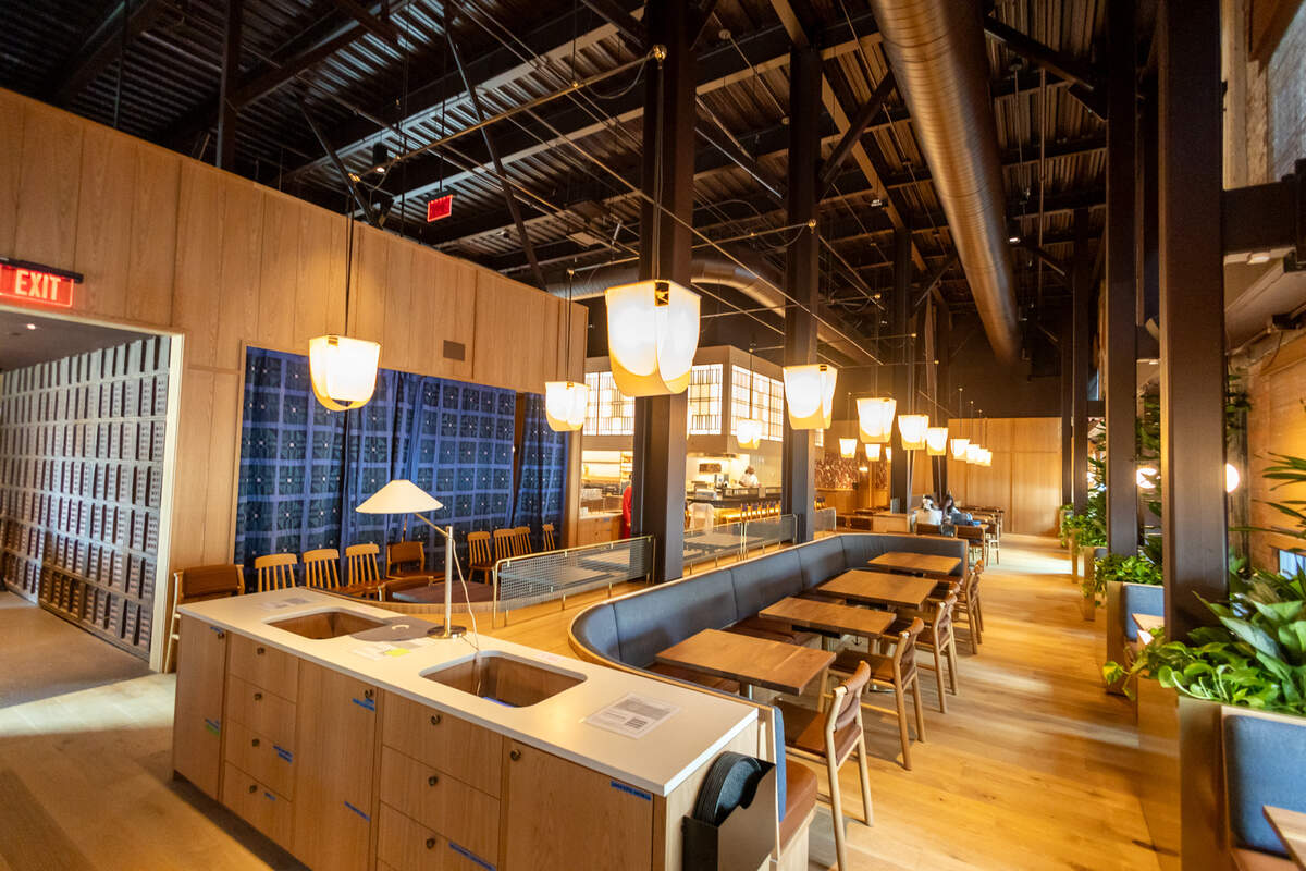 An interior shot looking down the center of the restaurant, showing mirrored seating arrangements with wooden tables and dark grey banquettes separated by a central wooden divider.