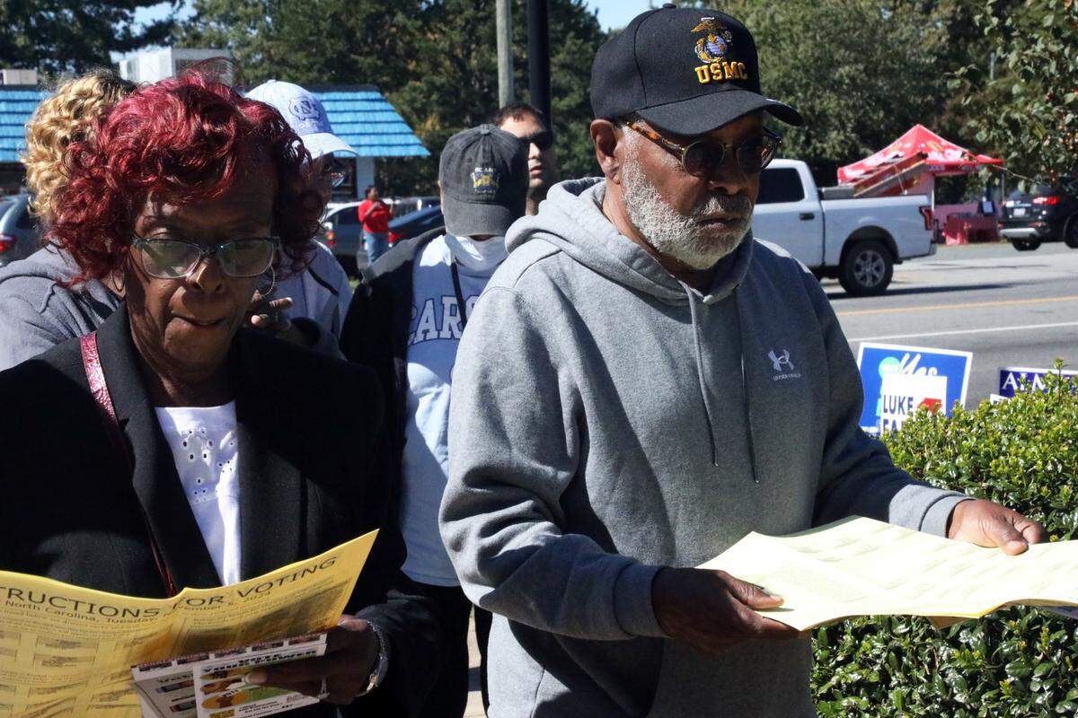 Early voters look over sample ballots with instructions for voting outside the polling place at the Allegra Westbrooks Regional Library in Charlotte, N.C. on October 17, 2024.