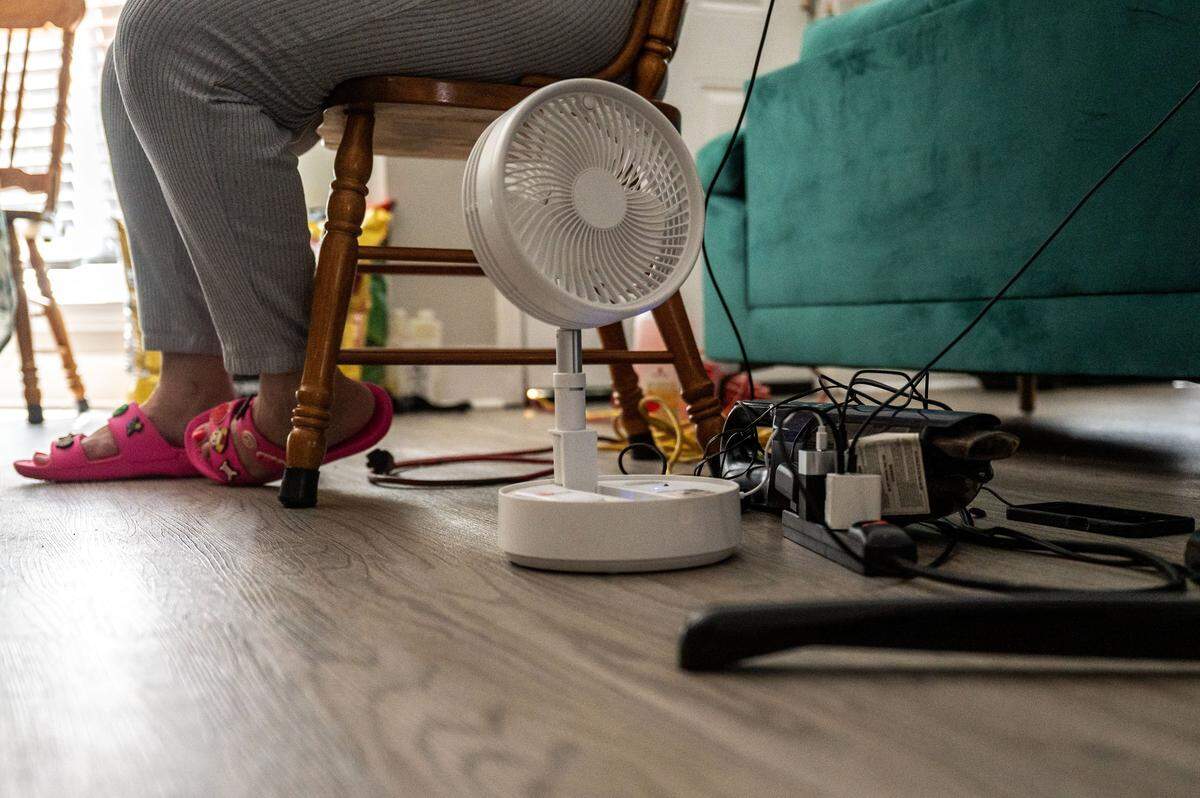 A backyard generator borrowed from a friend powers mini fans, phones and a handheld vacuum in Brandis Rogers’ living room on Aug. 1.