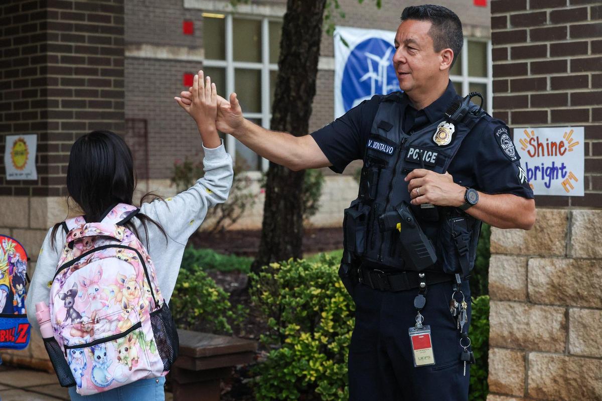 School resource officer Victor Montalvo, right, greets a student with a high-five as students arrive for the frist day of school at Waxhaw Elementary School on Monday, August 28, 2023.