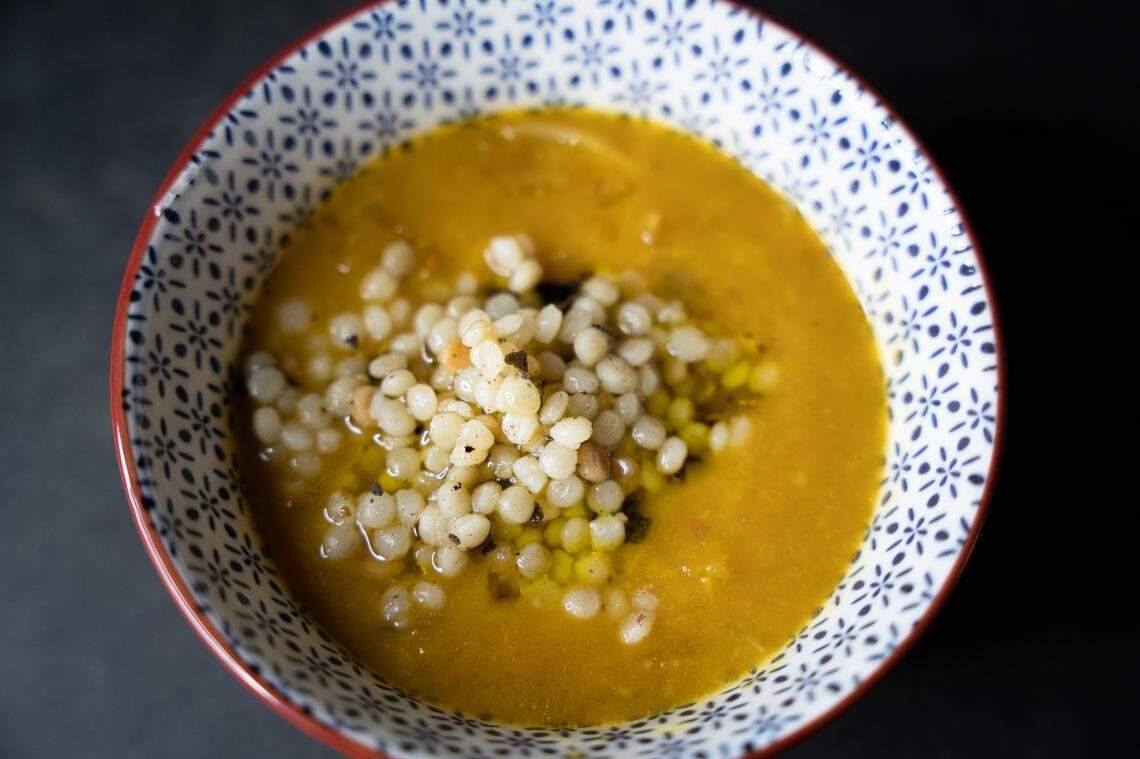 A bowl of roast pumpkin soup at center with a pile of couscous.