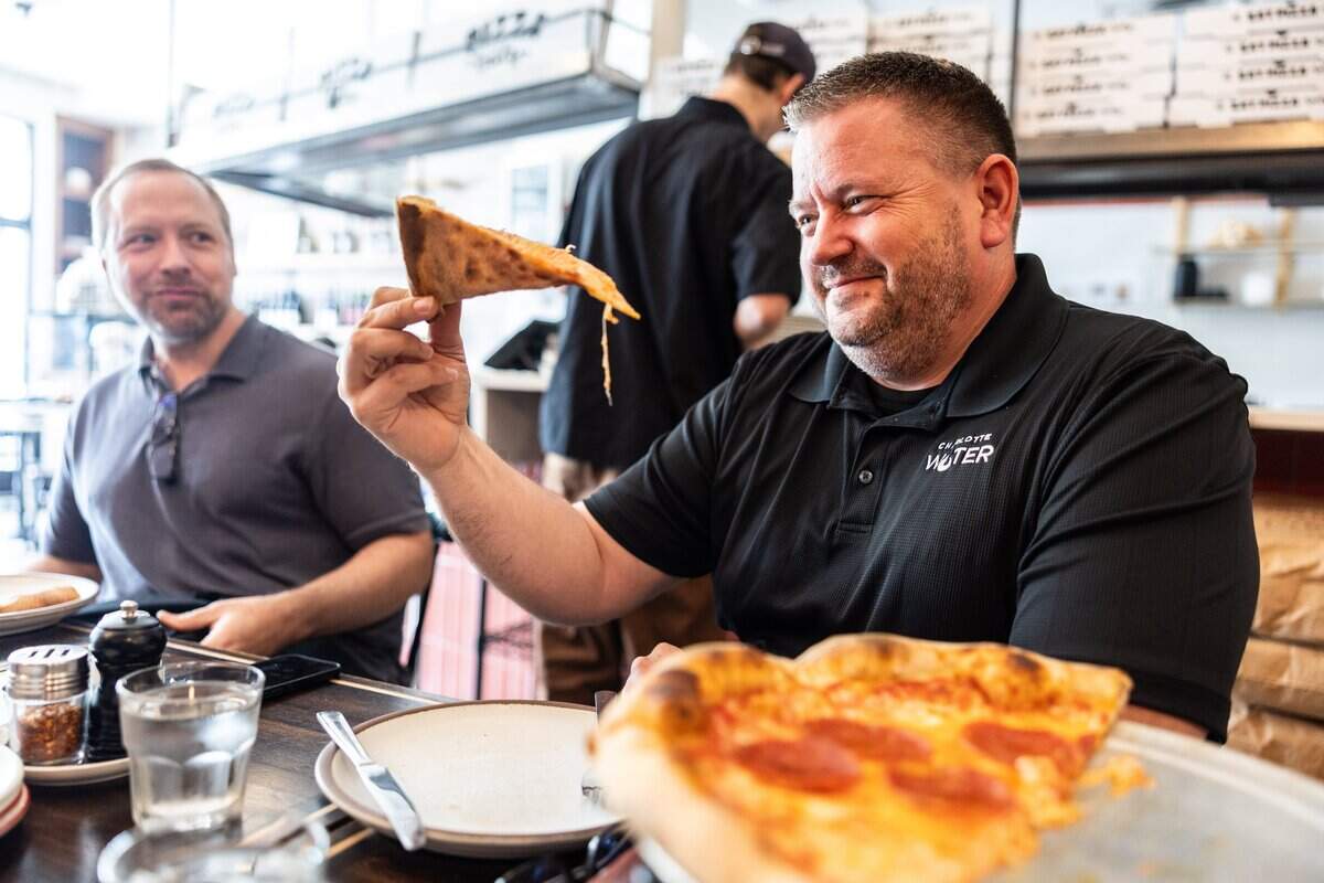 Matt Bryne smiles as he holds a slice of pizza at Pizza Baby in Charlotte, N.C., on Monday, April 13, 2026.