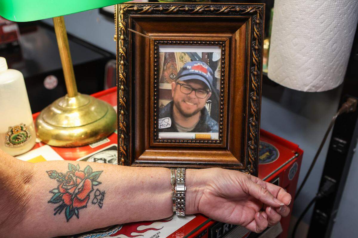 Kelly Kennedy rests her arm in front of a framed photo of her late son, Logan McAdams, showing a tattoo of a rose. The large bloom represents herself and the small bud on top represents Logan. Since his death, some of his family members and friends have gotten tattoos of his signature glasses and initials, as seen under Kennedy’s rose. And, Kennedy regularly visits his tattoo shop to chat with his co-workers and sit in his chair.