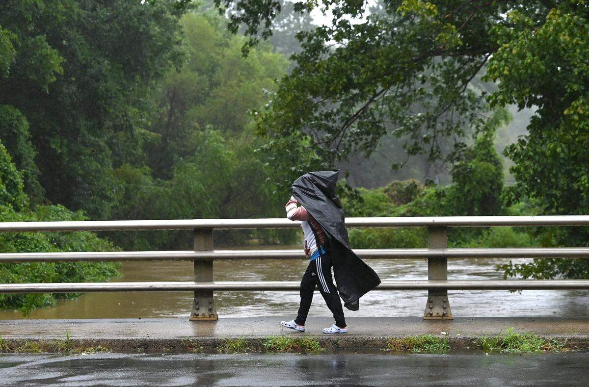 As heavy rain from Tropical Storm Debby fell, a Shamrock Drive resident in Charlotte crosses over a bridge covering Briar Creek, which overflowed its banks, on Thursday, August 8, 2024.