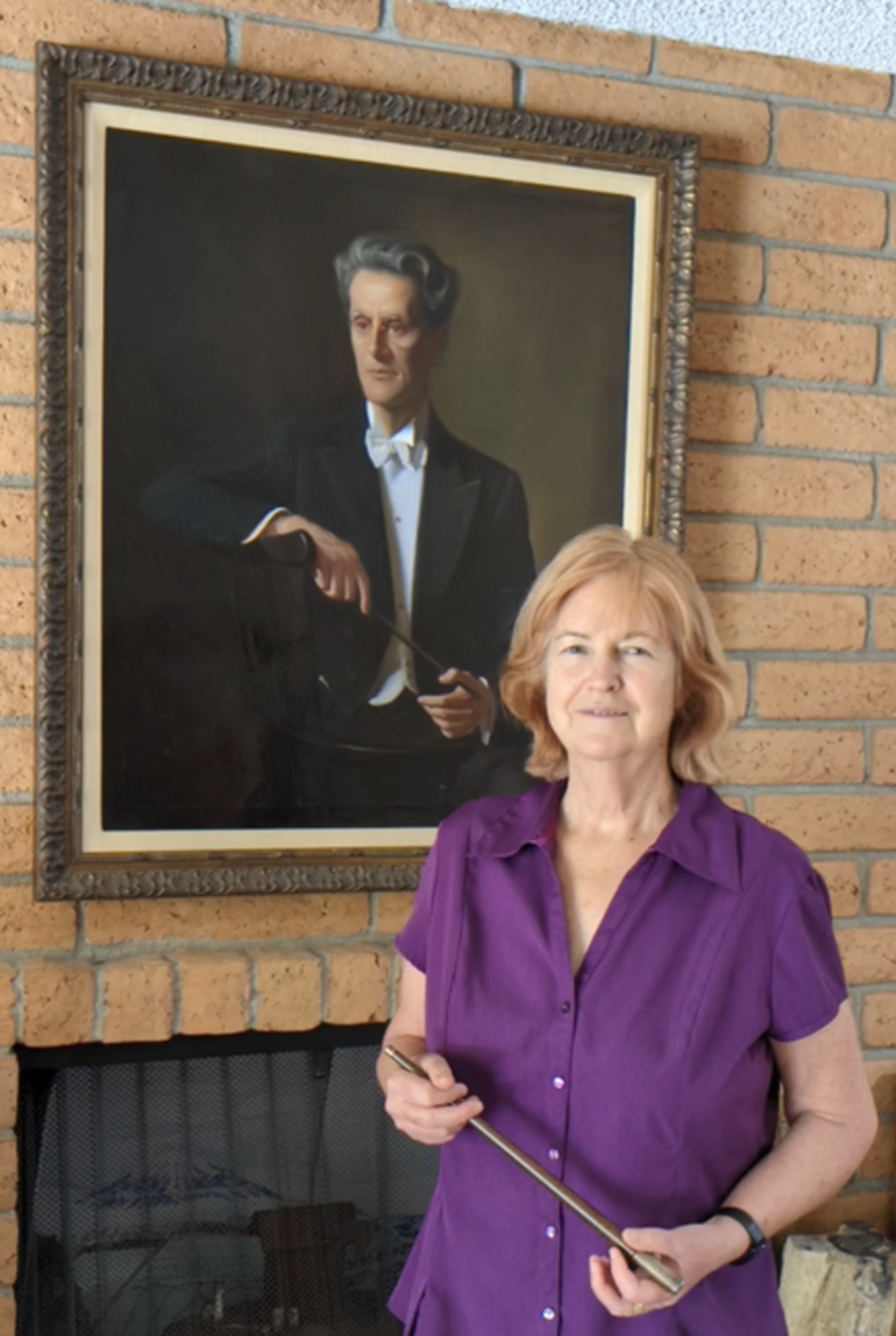 Katherine Roxlo holds the baton used by her grandfather, Guillermo S. de Roxlo, first music director of the Charlotte Symphony. She is in her Phoenix home with her grandfather’s portrait, painted by his contemporary Dayrell Kortheuer. Roxlo is donating a copy of the portrait to the symphony.