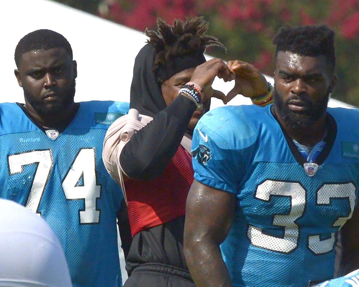 Even a day off from practice didn’t keep Carolina Panthers quarterback Cam Newton, center, from showing his love to fans as he stands between tackle Greg Little, left and running back Elijah Holyfield.