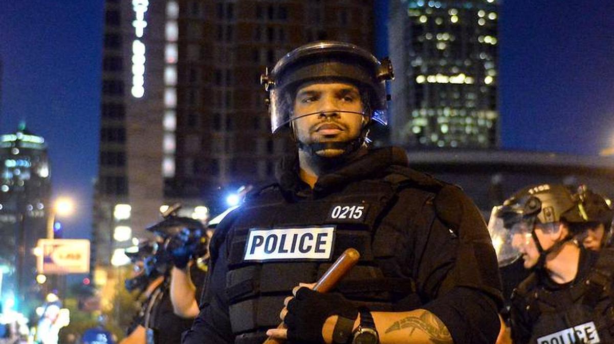 A CMPD officer stands watching protesters as other officers make an arrest in a parking lot along East Trade Street in Charlotte on Sunday night. Charlotte protesters were protesting the May 25 death of George Floyd at the hands of Minneapolis police.
