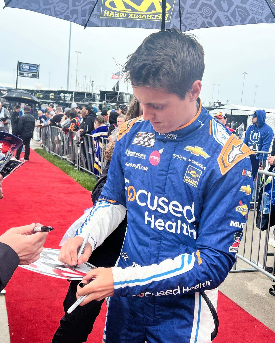May 5, 2024; Kansas City, Kansas, USA; NASCAR Cup Series driver Zane Smith (71) signs autographs under an umbrella during pre-race rain at Kansas Speedway.