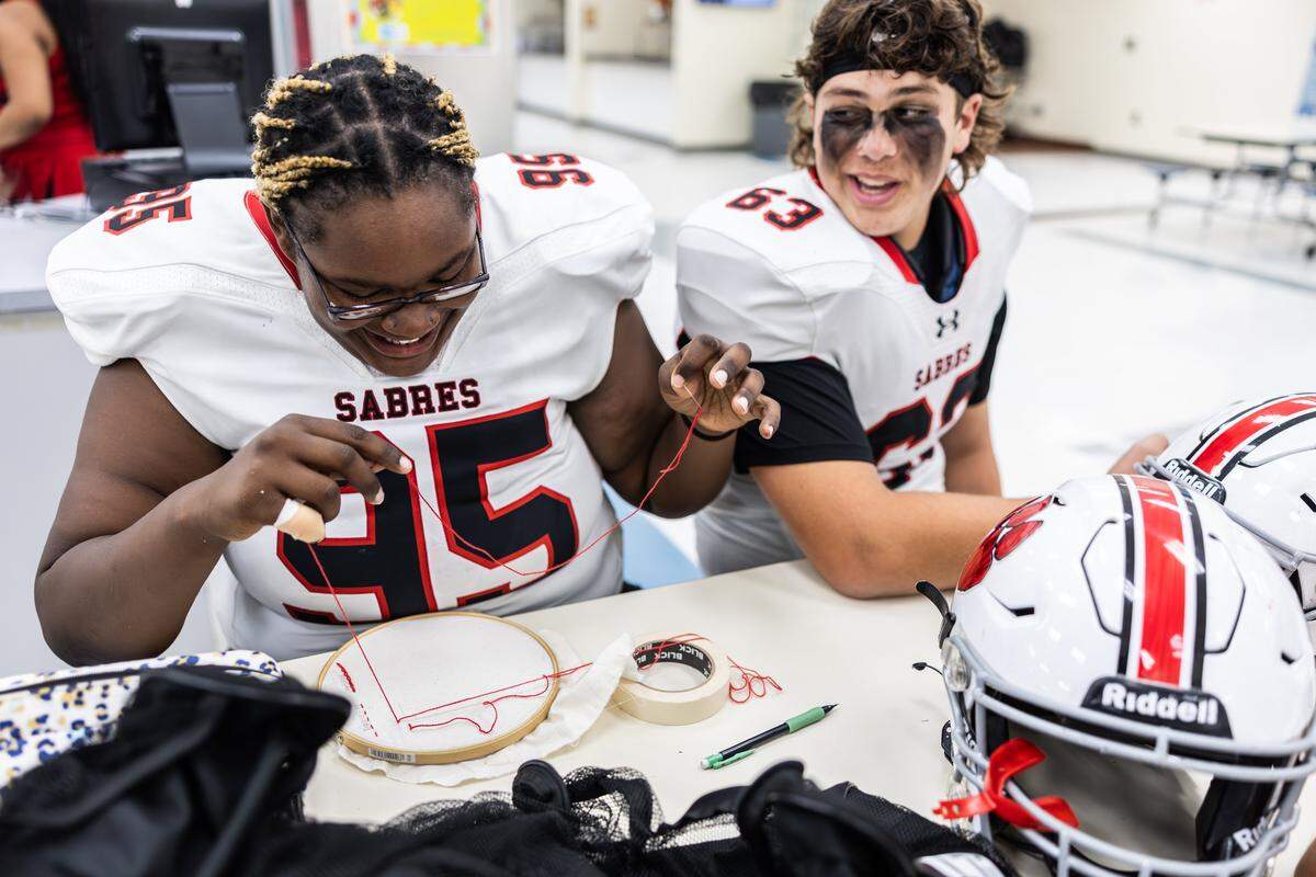 South Mecklenburg's female offensive lineman, Yazmine Beverly, left, works on an embroidery project during a weather delay before a game at Hopewell High School in Huntersville, N.C., on Friday, September 26, 2025.