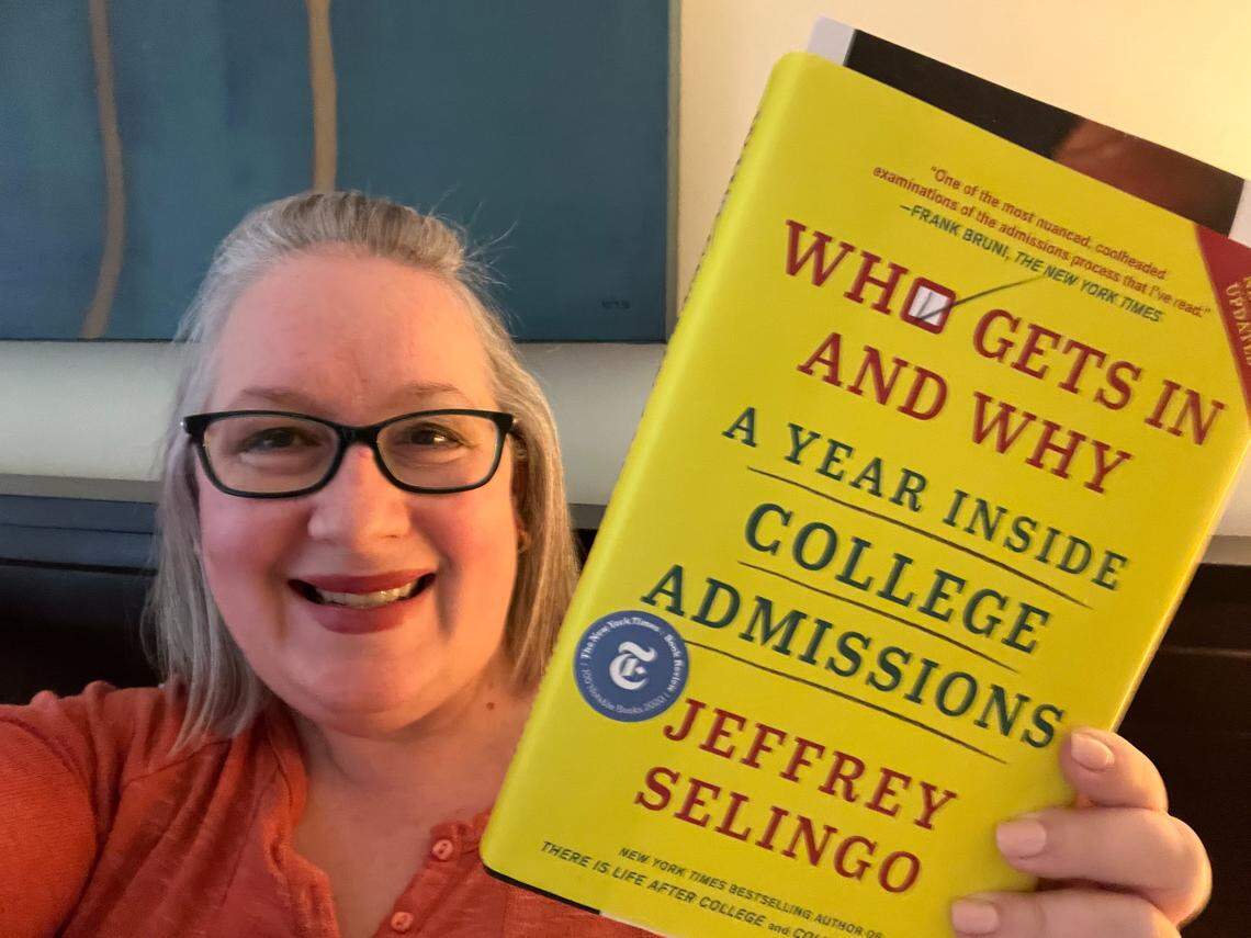 A smiling person with gray hair and black glasses holds up a bright yellow book titled, “Who Gets In and Why: A Year Inside College Admissions” by Jeffrey Selingo.