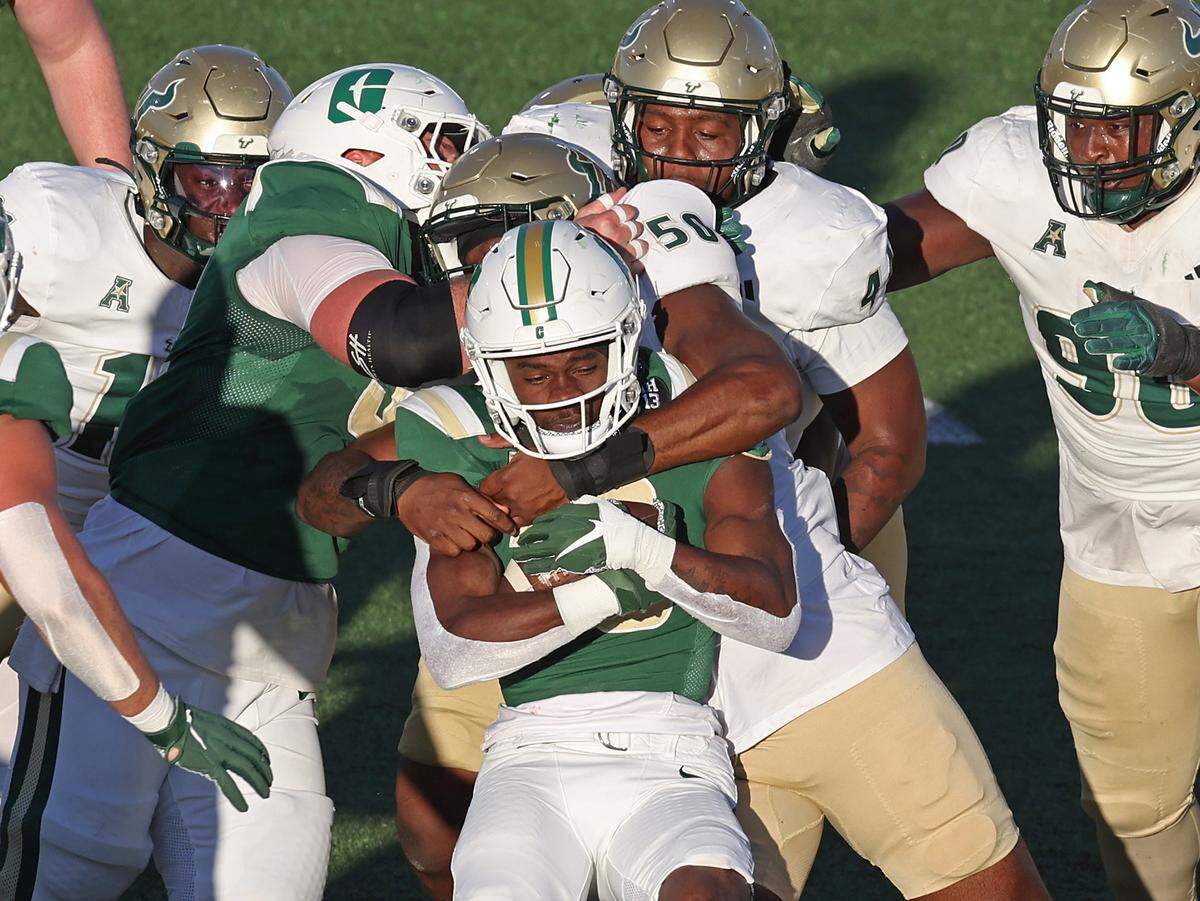 Charlotte 49ers running back Hahsaun Wilson, center, clutches the ball to his chest as South Florida defensive end Dinellson Exume attempts to make the tackle during action on Saturday, November 16, 2024 at Jerry Richardson Stadium.