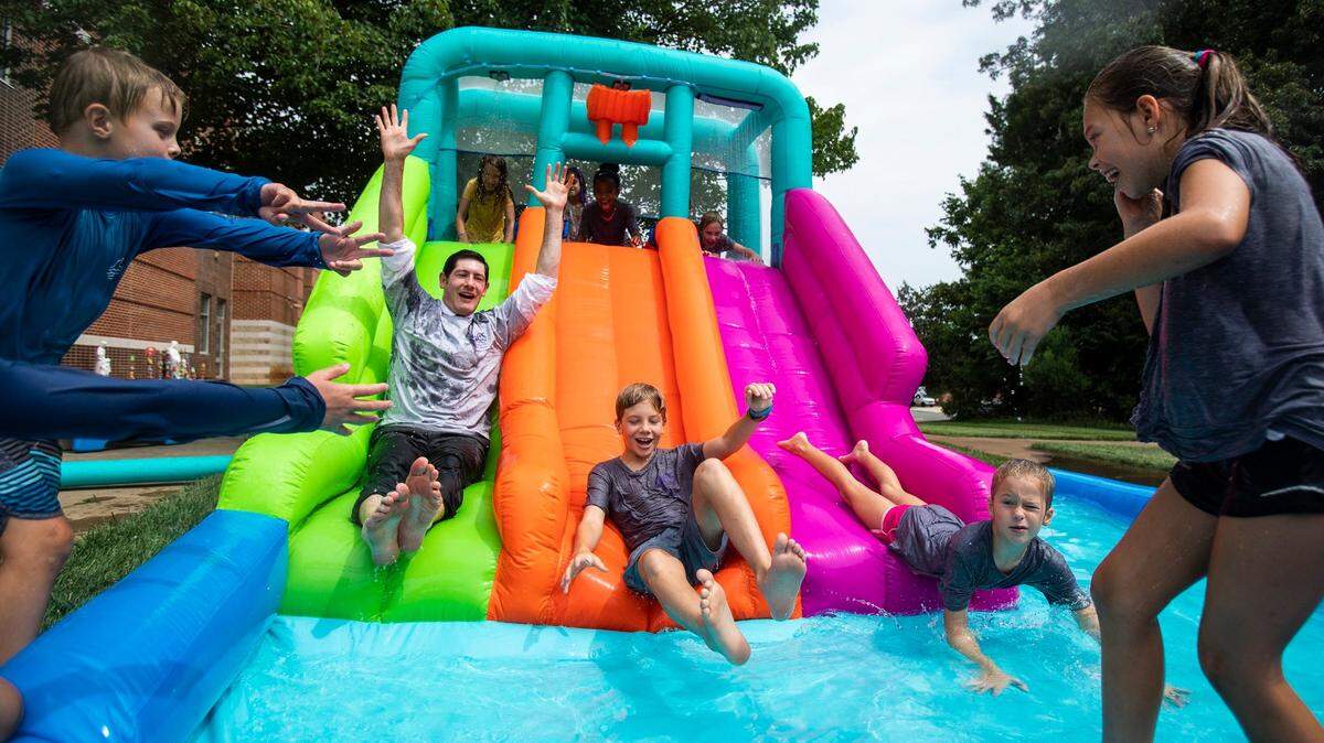Dr. Gregory Monroe, second from left, joins kids in going down an inflatable water slide at a summer camp at St. Matthew Catholic School in 2022.