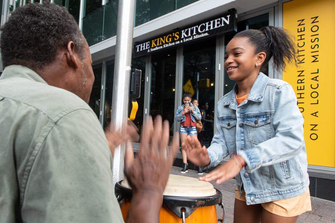Joel Burks, 58, plays a conga drum on the corner of South Church and West Trade streets with a young spectator as her mother films them together on Wednesday, June 29, 2022 in uptown Charlotte, N.C. Burks says he feels his music helps him connect with others and spread positivity.