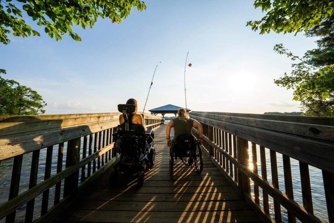 Two women, one using a motorized wheelchair and the other a manual wheelchair, make their way down an ADA-compliant fishing pier at Ramsey Creek Park on Lake Norman. Ramsey Creek Park features accessible amenities, including fishing piers, trails, and picnic areas, ensuring outdoor recreation for all visitors.