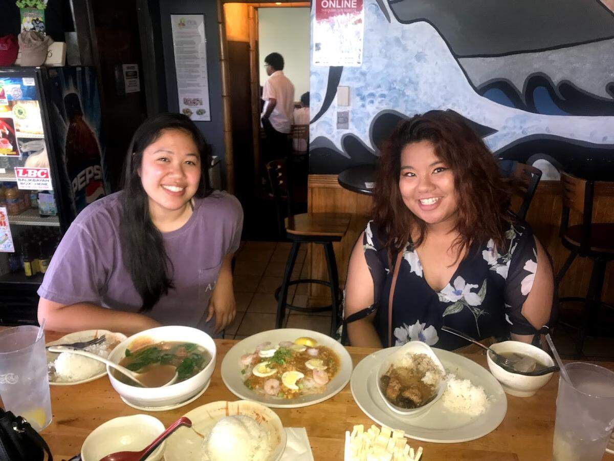 Gloriana Bernabe (right) and her friend enjoy a meal at Joel’s Asian Grill. The soup on the left is sinigang, in the middle is a noodle dish called pancit palabok with ground pork, shrimp, eggs and pork cracklings. At right is chicken adobo, often considered the national dish of the Philippines.