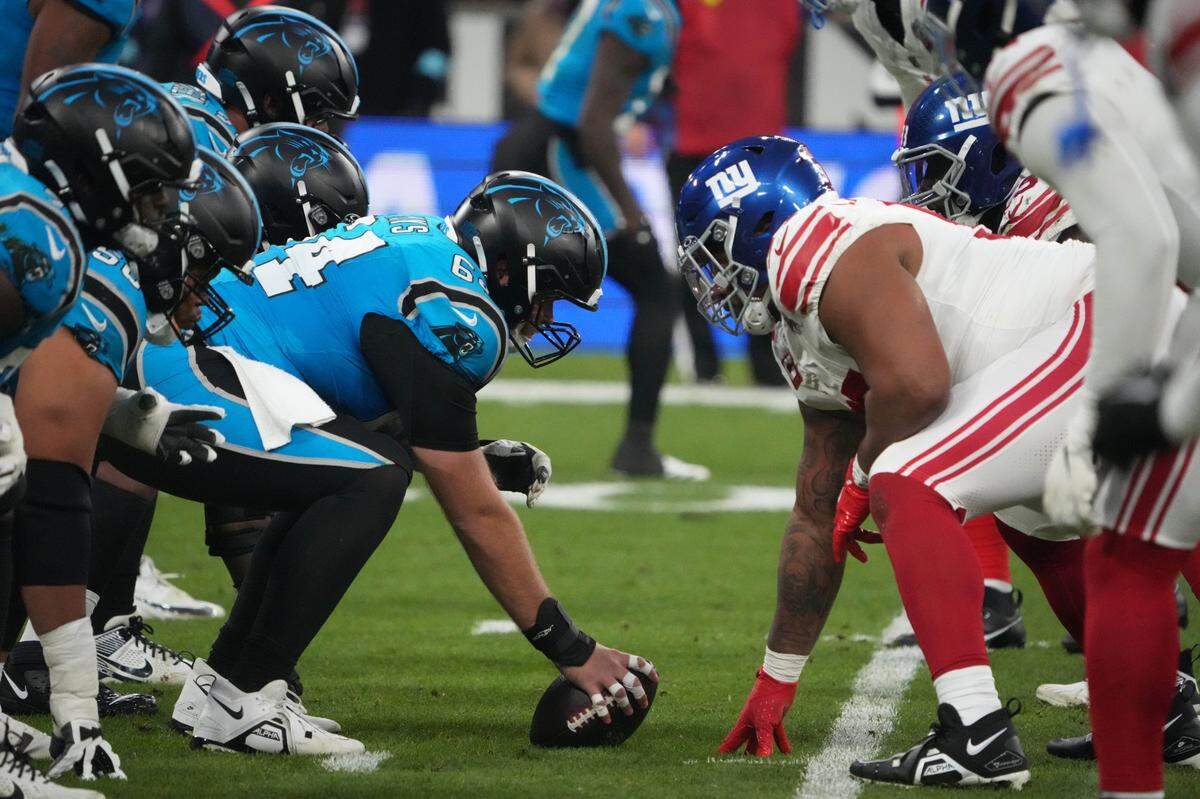 Nov 10, 2024; Munich, Germany; Helmets at the line of scrimmage as Carolina Panthers guard Cade Mays (64) snaps the ball against the New York Giants in the first half during the 2024 NFL Munich Game at Allianz Arena. Mandatory Credit: Kirby Lee-Imagn Images
