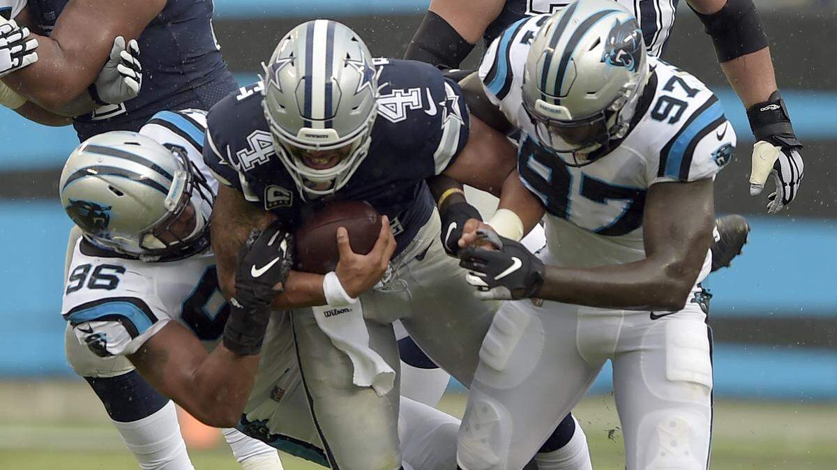 Dallas Cowboys quarterback Dak Prescott (4) is tackled by Panthers defensive ends Wes Horton (96) and Mario Addison (97) during the second half on Sunday at Bank of America Stadium.