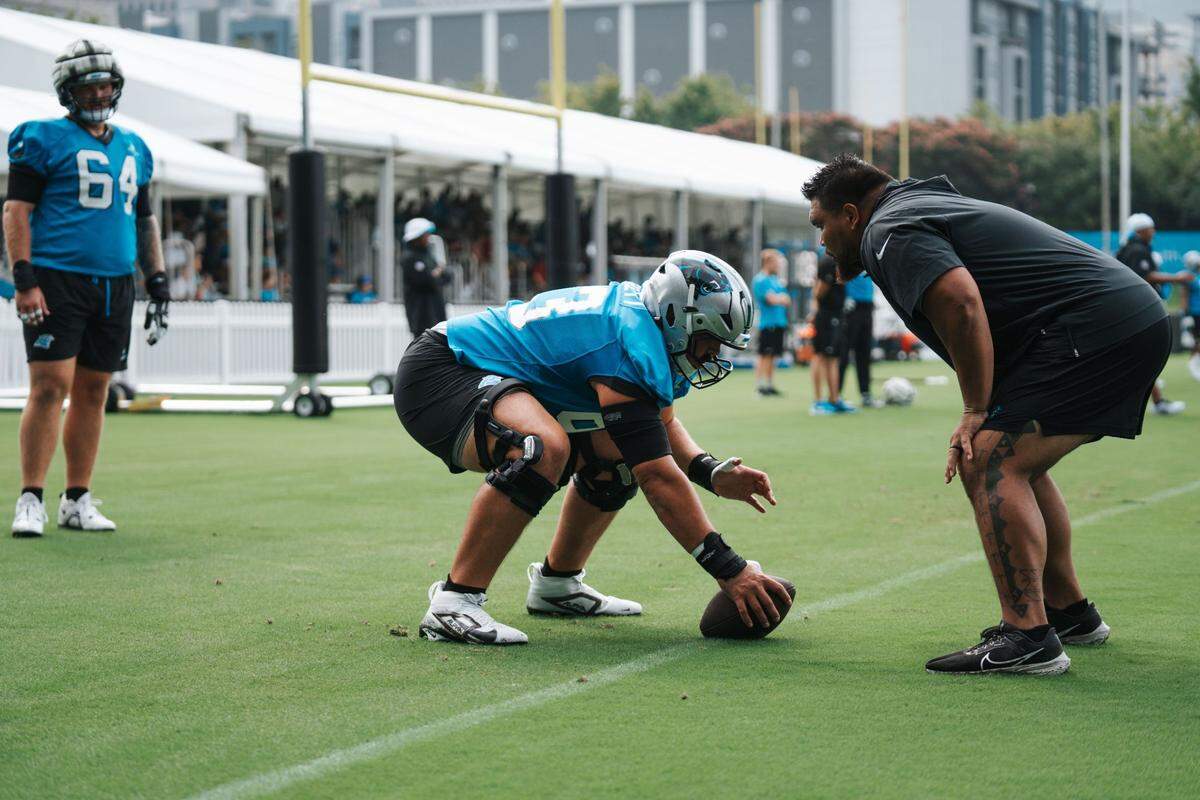 Carolina Panthers assistant offensive line coach Keli’i Kekuewa leads center Austin Corbett through a snapping drill during practice on the fields outside of Bank of America Stadium.