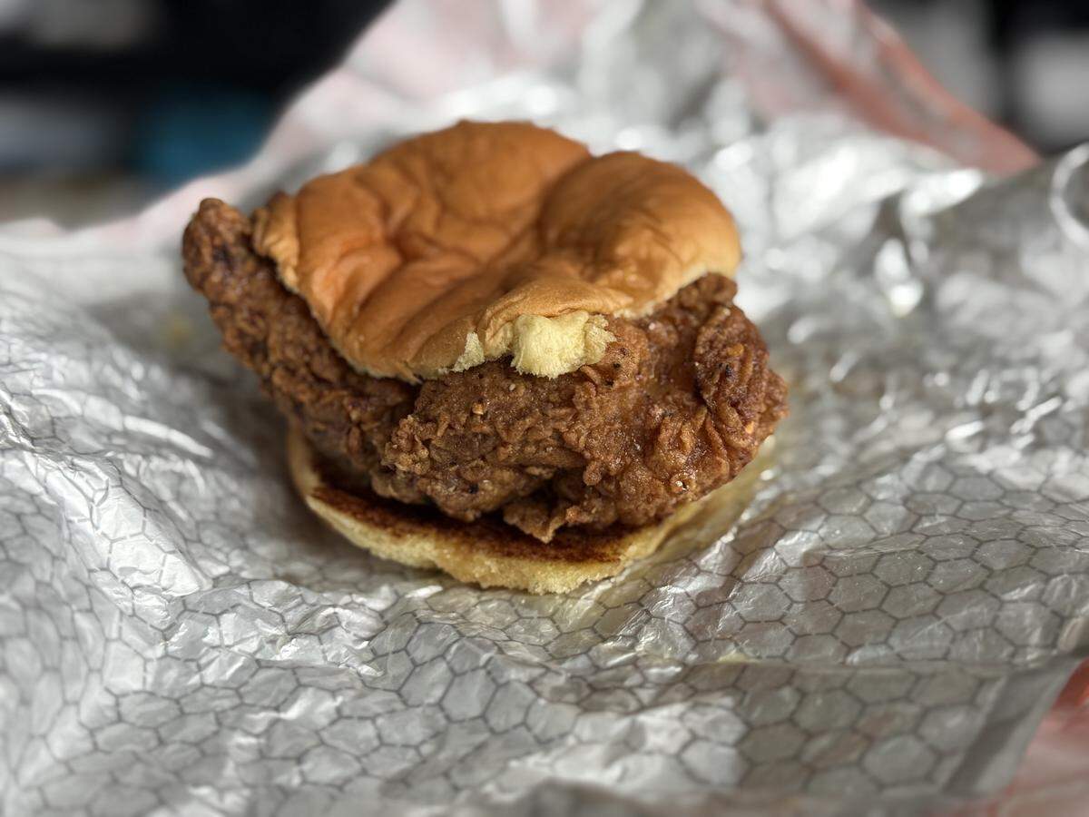 A close-up shows a sandwich wrapped in Surefire-branded orange paper resting on a plate, followed by the unwrapped fried chicken sandwich on a soft, toasted bun.