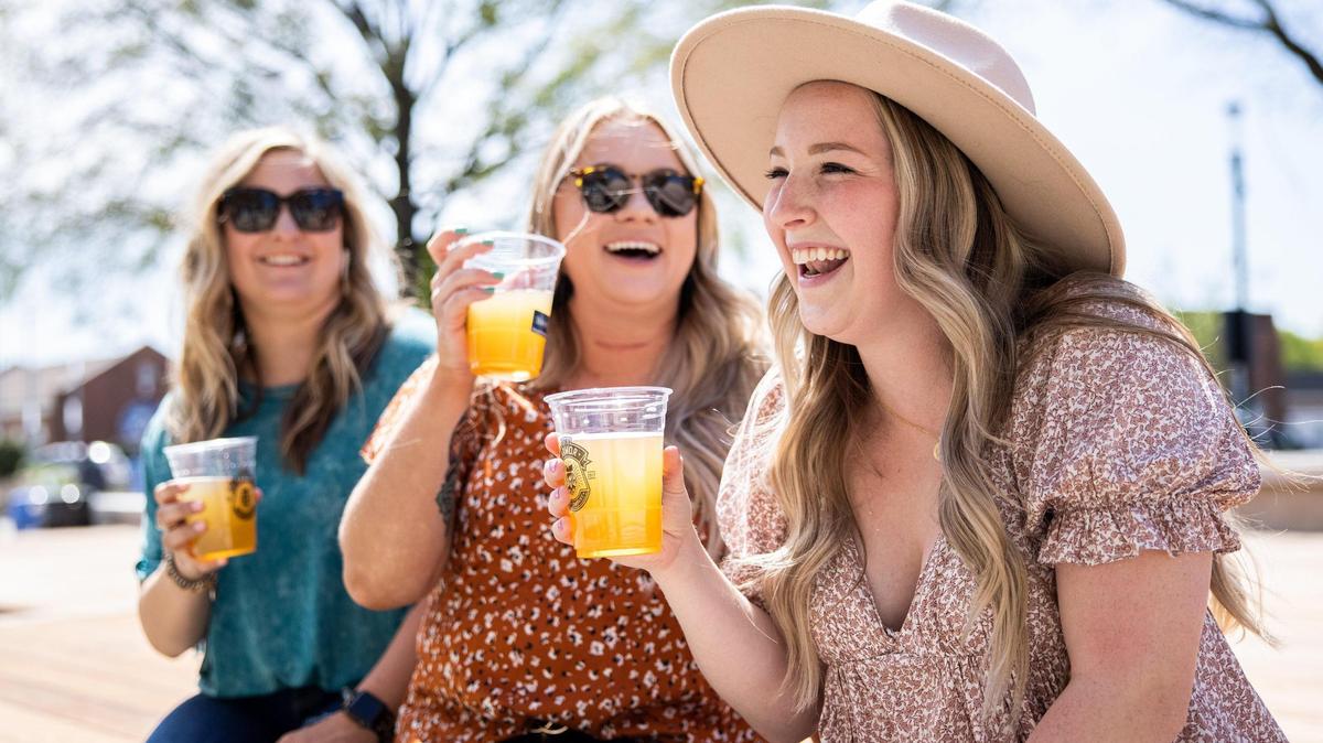 Taylor Cranford, from left, Nicole Smith and Peyton Nance share a laugh over a beer April 15 in the social district of downtown Kannapolis.