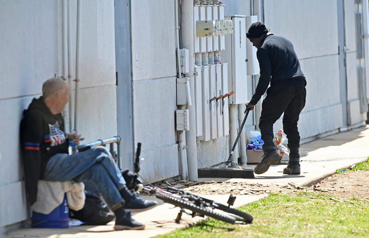 Kenny cleans the area behind a small row of businesses lining South Boulevard near Woodlawn Road area as Lefty looks on.
