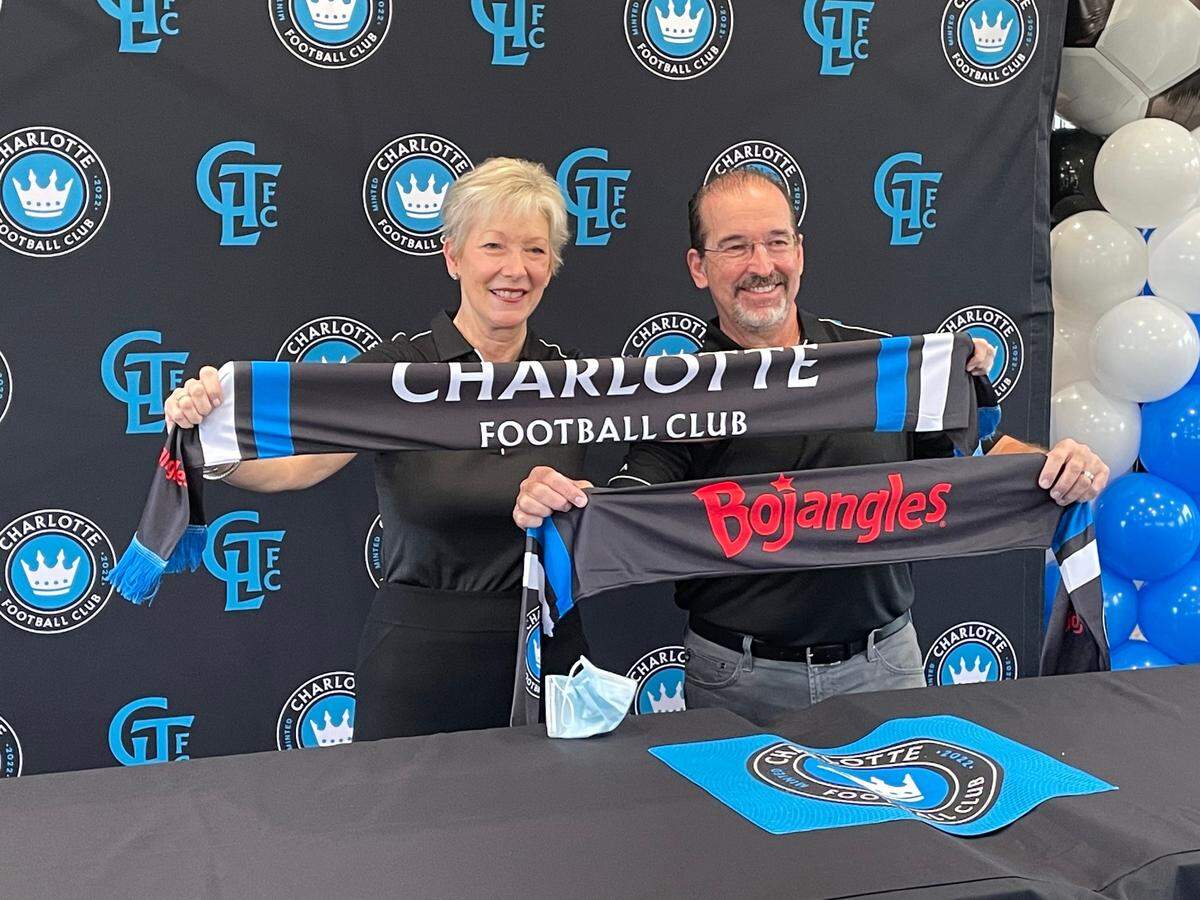 Bojangles restaurant supports the Charlotte community in several ways, including a partnership with Charlotte FC professional soccer team. Shown in 2021, CMO Jackie Woodward and CEO Jose Armario pose with Charlotte FC scarves as the team’s official tailgate partner.