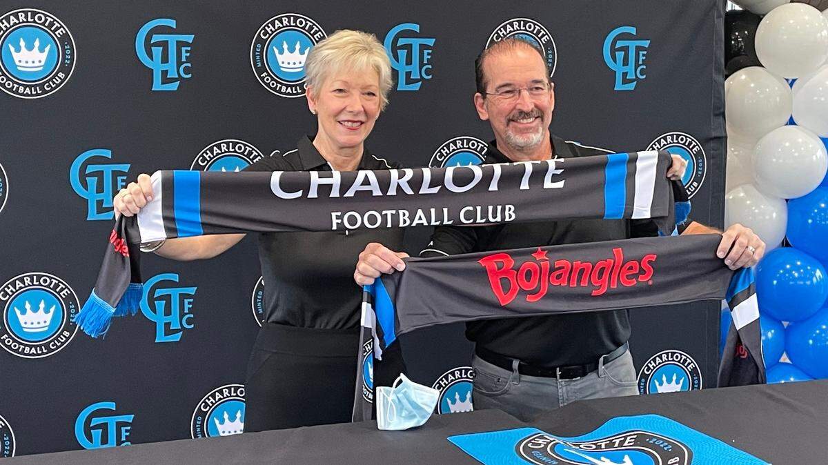 Bojangles CMO Jackie Woodward and CEO Jose Armario pose with Charlotte FC scarves at a West Trade St. restaurant location to commemorate the launch of a long-term partnership between Charlotte FC and Bojangles as the team’s official tailgate partner.