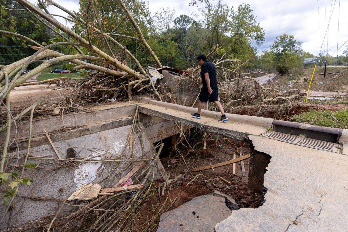 A man crosses a narrow section of flood damaged bridge in Swannanoa on Sunday, Sept. 29, 2024. The remnants of Hurricane Helene caused widespread flooding, downed trees, and power outages in western North Carolina.