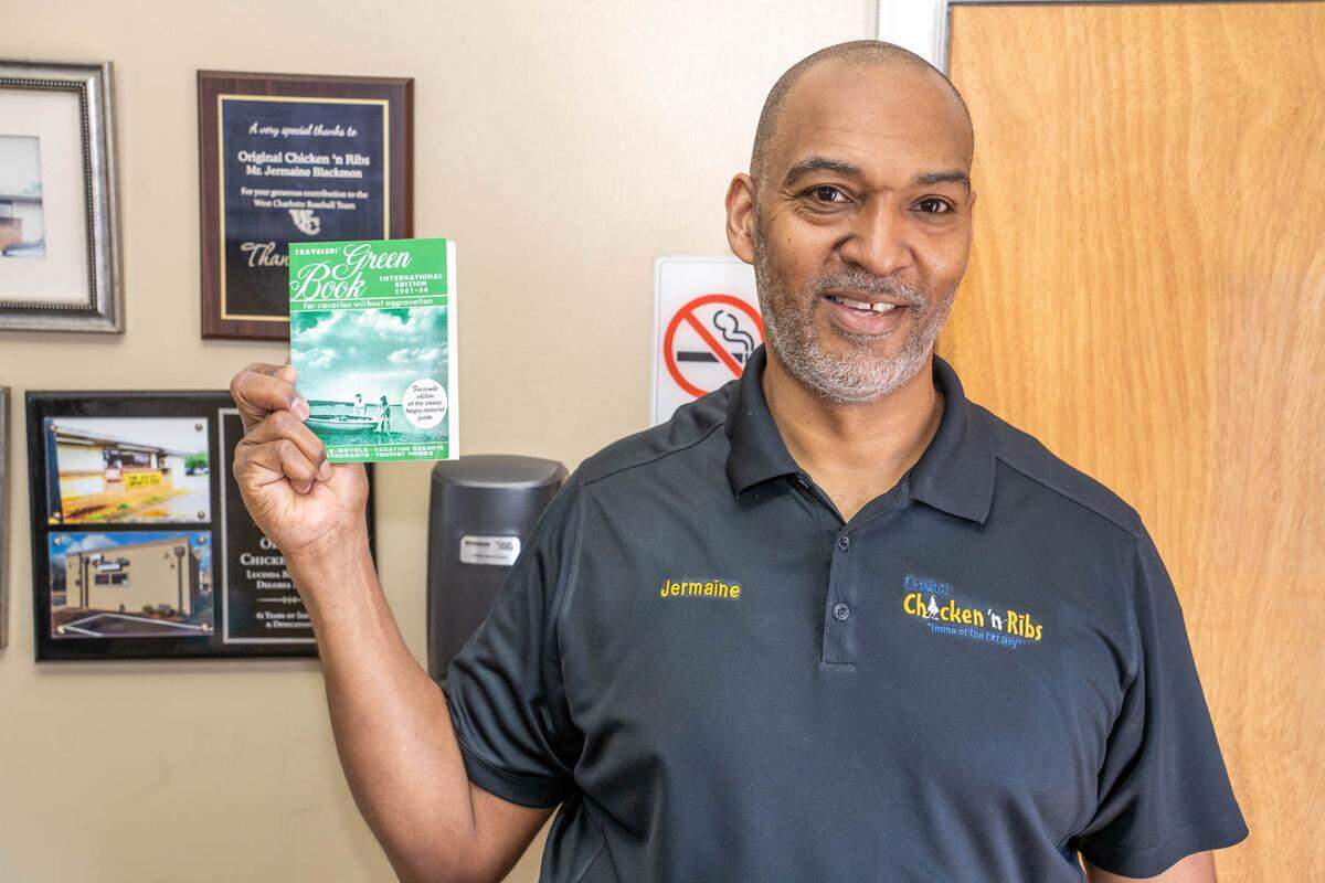 Jermaine Blackmon, the third generation owner of Original Chicken ‘n Ribs, holds a facsimile edition of “The Negro Motorist Green Book” — a guidebook that let Black travelers know of gas stations, hotels, restaurants and other establishments they could visit safely. Original Chicken ‘n Ribs is the only restaurant listed in Charlotte that remains open.