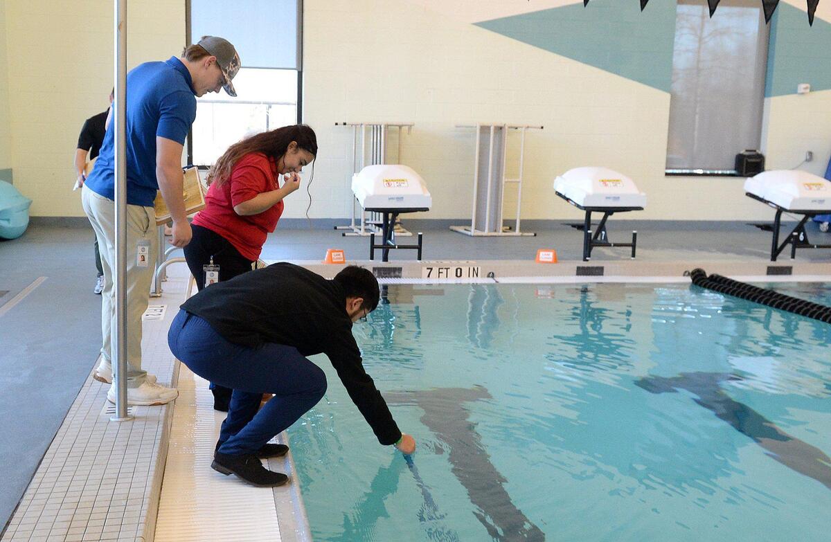 (L to R) Peyton Mincey, 21, Angelica Cabrera , 23, and Angel Cabrera Paulino, 20, try to stay dry to retrieve a murder mystery clue they’ve spotted in the deep end of the Eastway Regional Recreation Center lap pool. Saturday, Dec. 07, 2024.