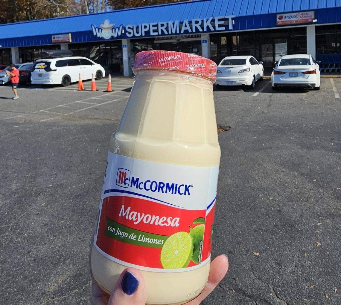 A jar of McCormick Mayonesa con Jugo de Limones (mayonnaise with lime juice) is held in the foreground, obscuring the lower half of the blue-and-white “WOW SUPERMARKET” sign visible in the background.
