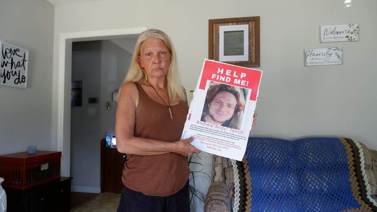 A mother standing in a living room, holding a poster.