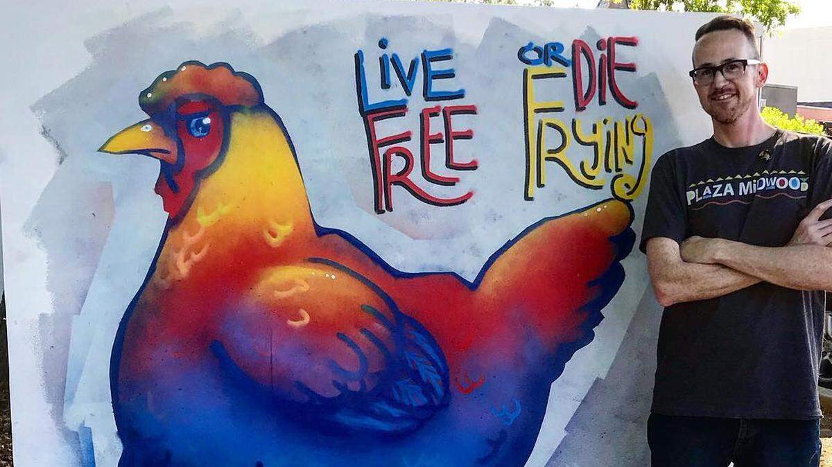 Mike Wirth stands in front of his Live Free or Die Frying mural after painting it live last April at the Boom festival in Plaza-Midwood.