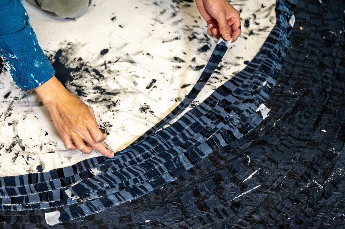 Kenny Nguyen, a Charlotte based artist, dips strips of silk into layers of paint before lying them onto of each other on a canvas in his Concord studio in Concord, NC, Tuesday August 1, 2025.