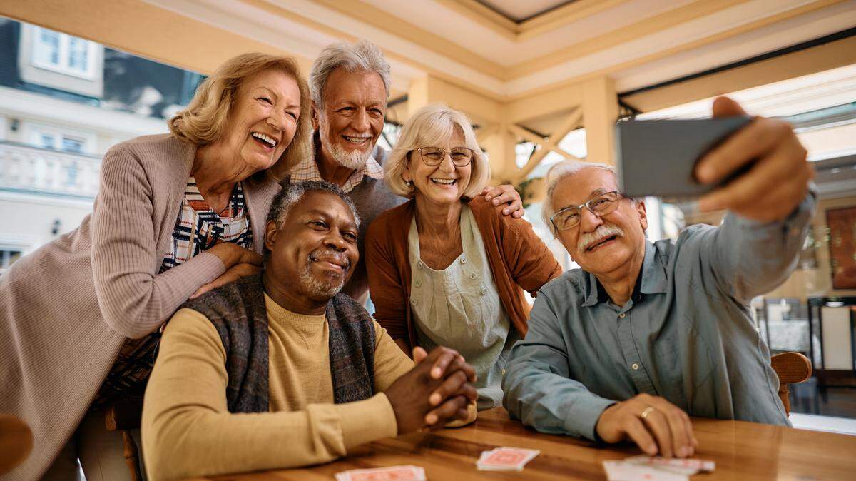 Group of happy senior people taking selfie with cell phone in nursing home.