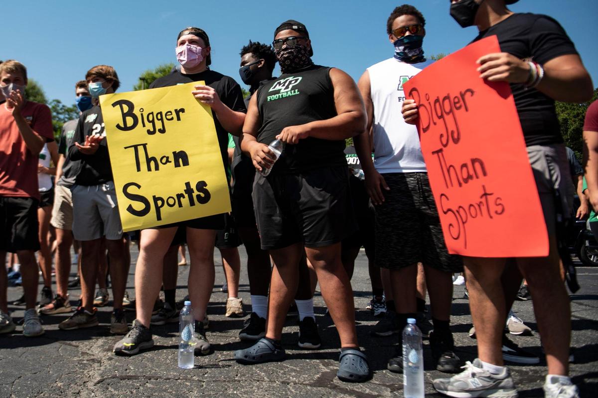Student-athletes hold “Bigger Than Sports” signs during a rally calling for Charlotte-Mecklenburg Schools to allow fall sports and practices in the parking lot of CMS’ Central Office in Charlotte on Wednesday.