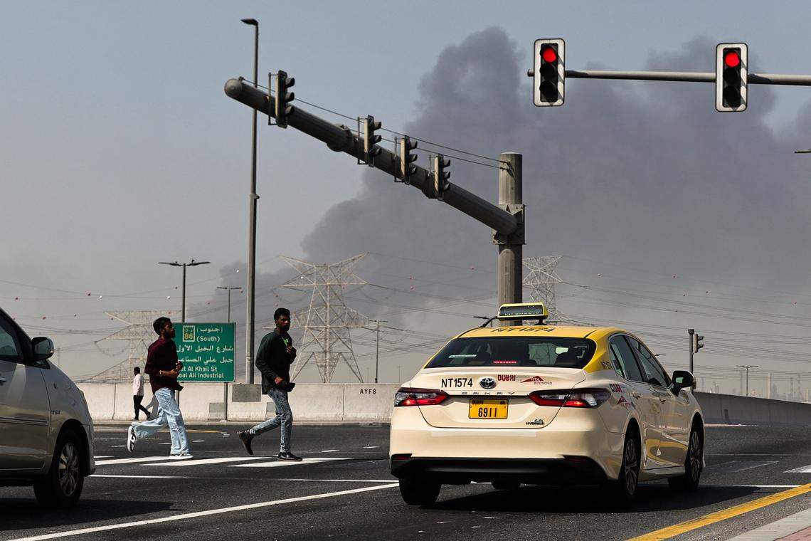 People cross a street as smoke rises from the site of a reported Iranian strike in Dubai on March 1, 2026. 