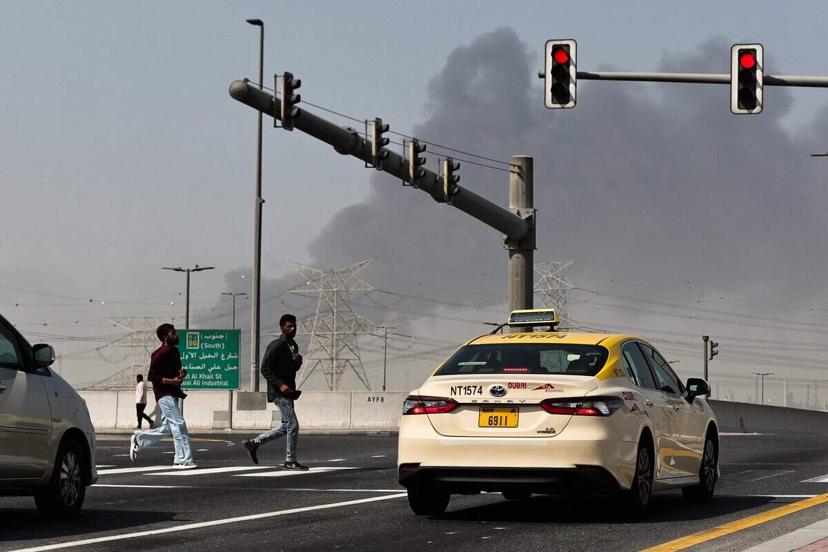 People cross a street as smoke rises from the site of a reported Iranian strike in Dubai on March 1, 2026. 