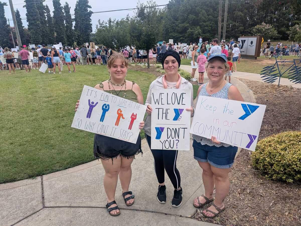Members of the Brundick family, from left, Saturn, Rachael and their mom, Gina, join hundreds in south Charlotte on Sunday to protest the sale of the Morrison Family YMCA.
