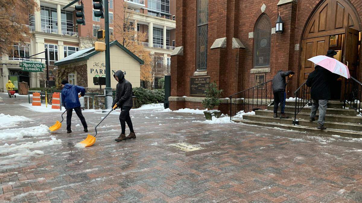 People scrape away snow and ice outside St. Peter Catholic Church in uptown Charlotte before the 9 a.m. Mass on Sunday. Many other churches around Charlotte canceled services after inches of snow fell in the region.