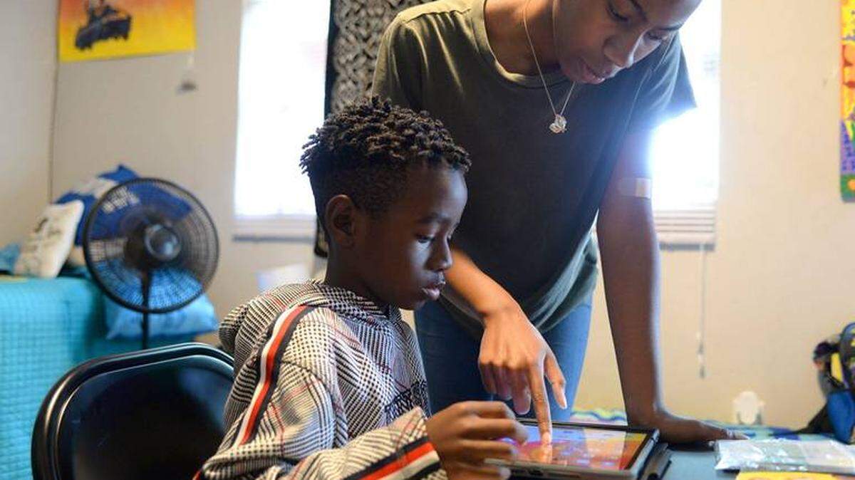 Daniel Feaster, left, works on a school lesson as his sister, D’erra Moise, right, offers guidance on Aug. 17, 2020. Daniel, a CMS second grader, is doing remote learning from the family’s home.