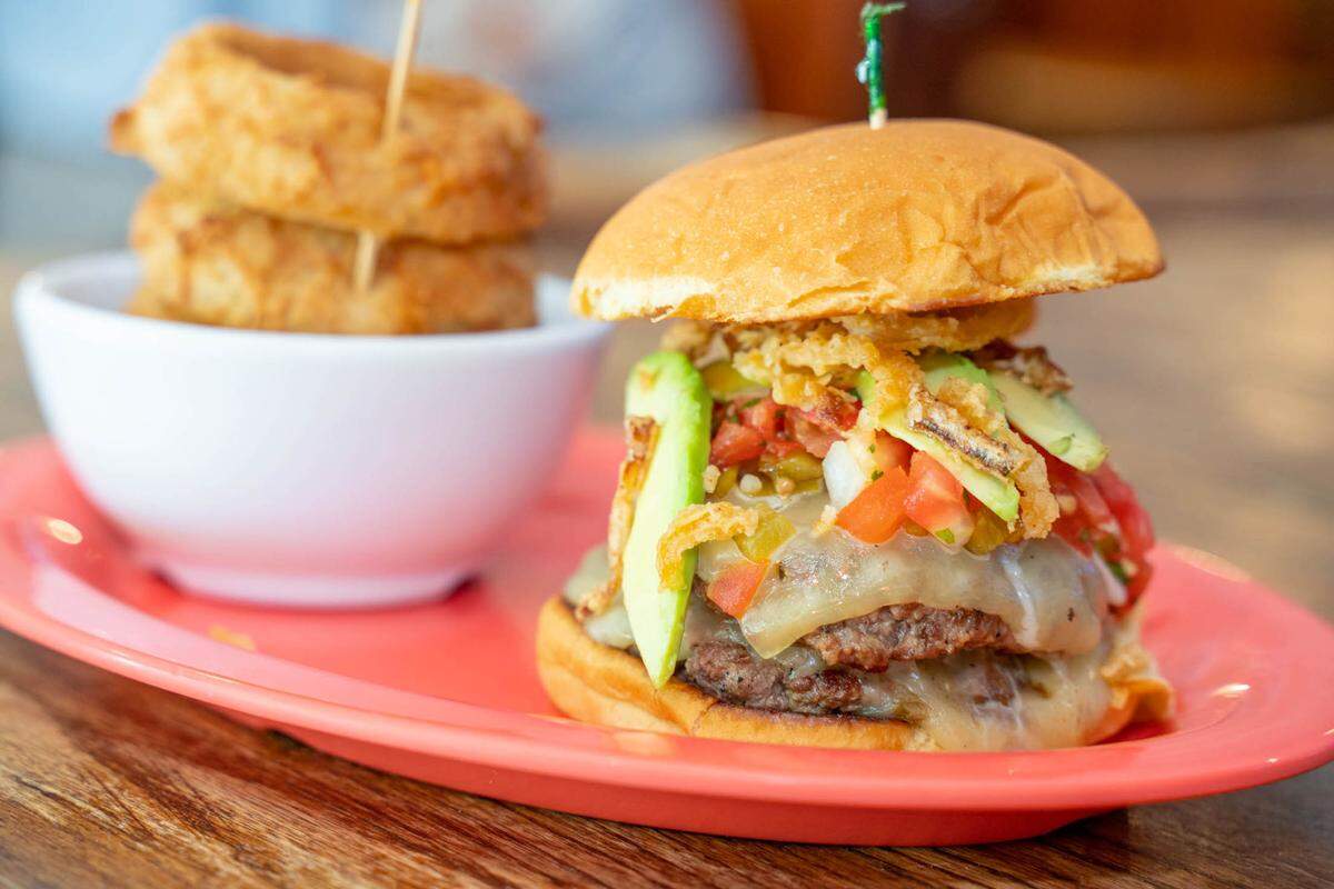 An avocado burger at Providence Road Sundries has salsa, onion straws and pepperjack cheese on it with a side of onion rings.