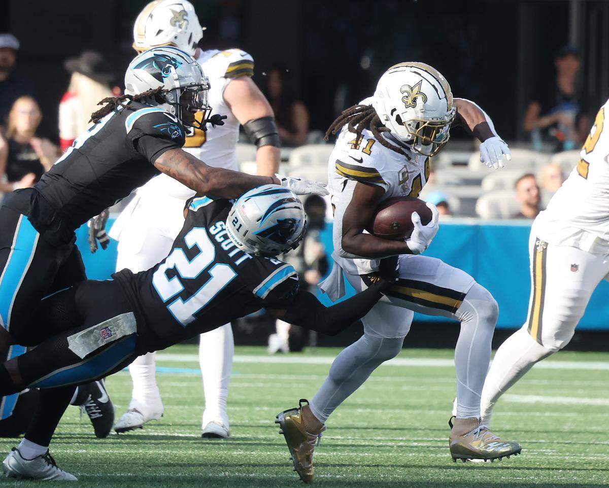 New Orleans Saints running back Alvin Kamara carries the ball as Carolina Panthers safety Nick Scott (21) and cornerback Jaycee Horn go for the ball Sunday, Nov. 9, 2025 at Bank of America Stadium in Charlotte.