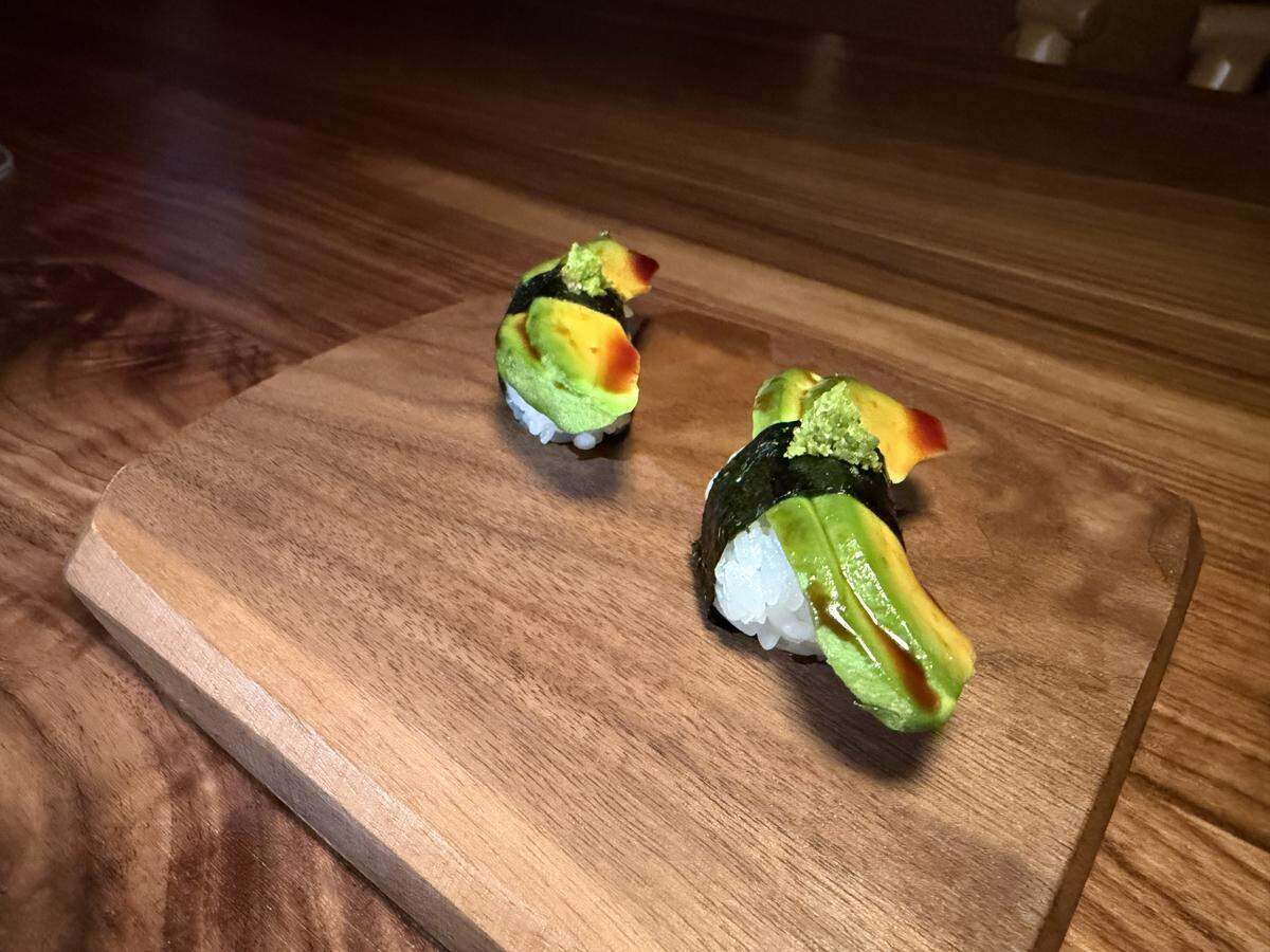 Two pieces of avocado nigiri are elegantly presented on a raised, light-wood serving block (geta).