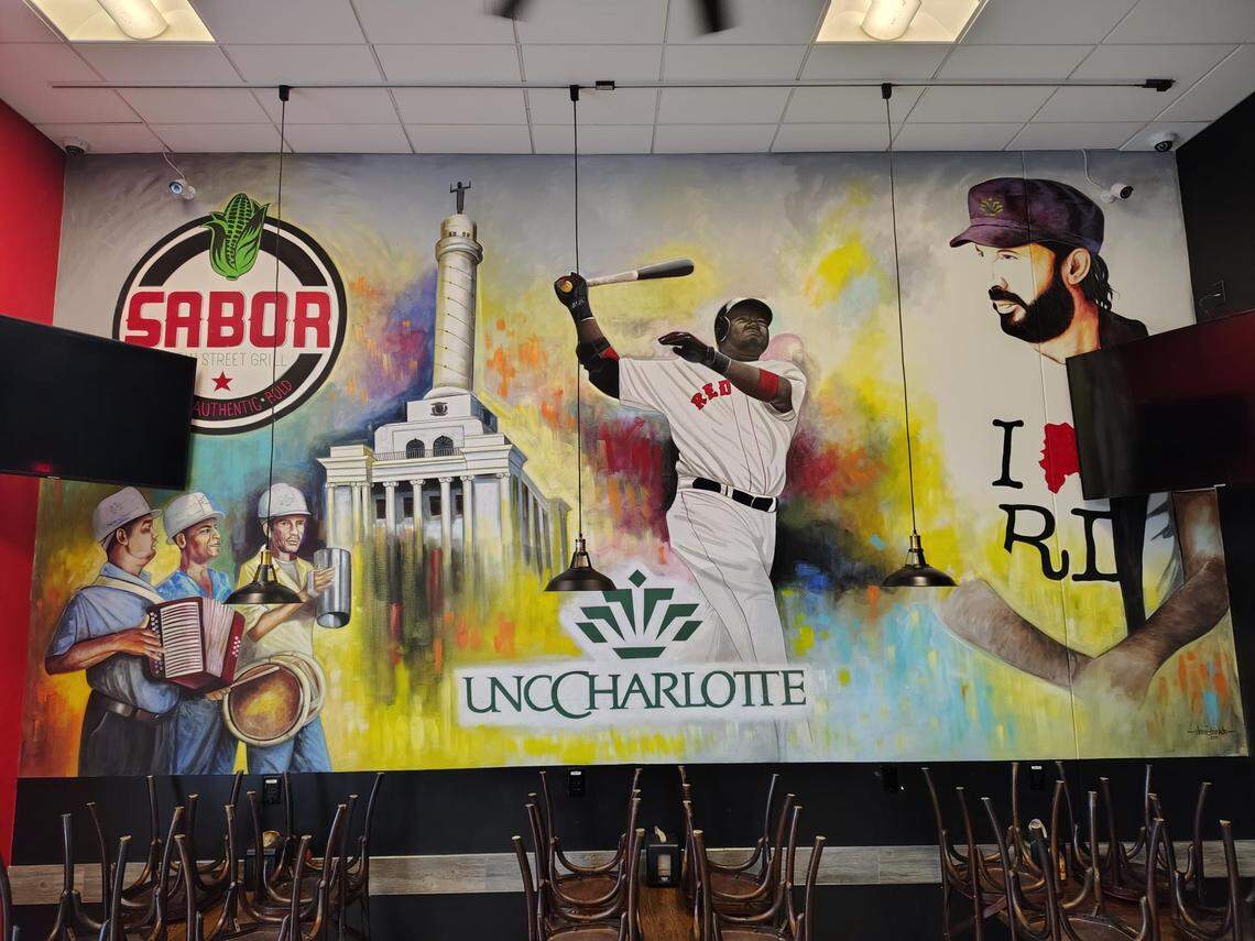 A wide shot of a multi-paneled, colorful mural inside a restaurant, which appears to be closed. The mural is a collage of images including a restaurant logo, Latin musicians, a historic building, a baseball player at bat, the UNC Charlotte logo, and a portrait of a man, all rendered in a vibrant, painterly style.