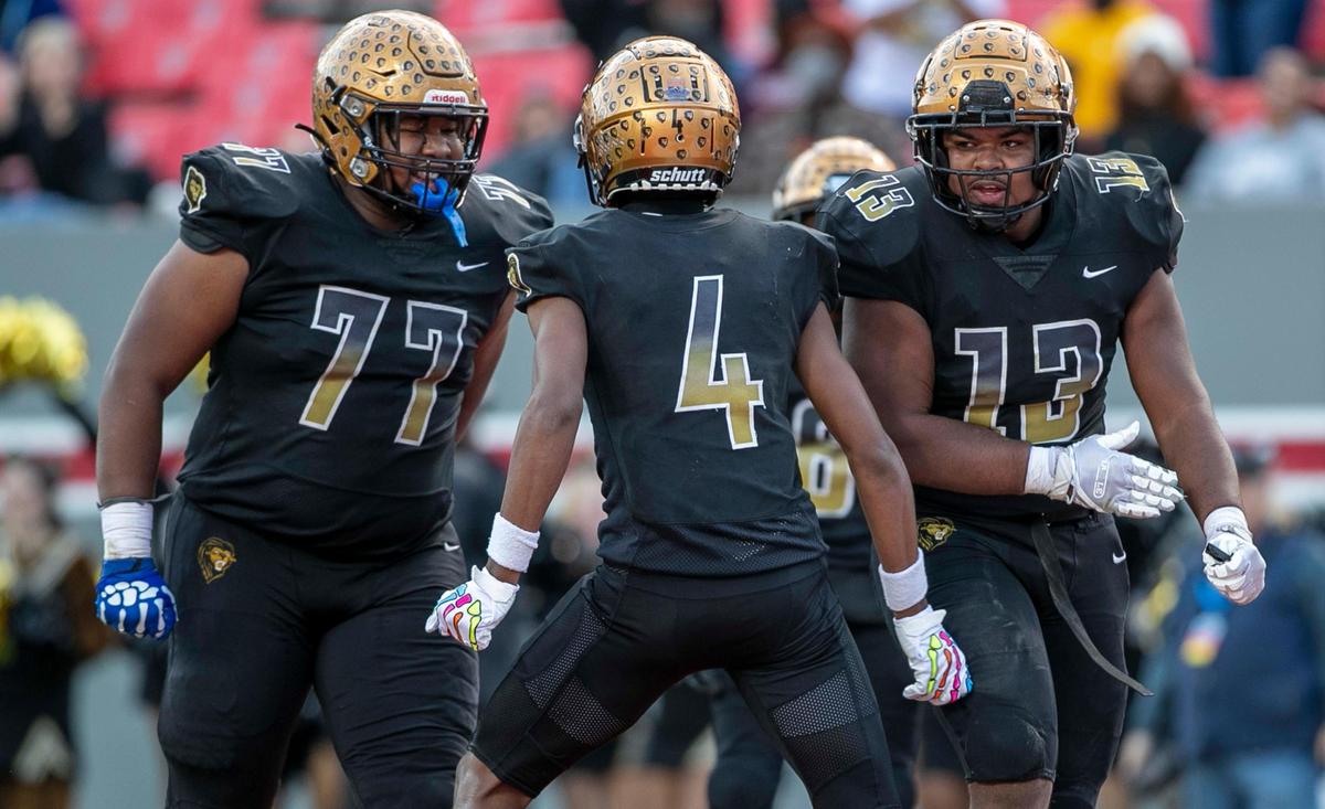 Shelby’s Ja’Keith Hamilton (4) celebrates with teammates Justyn Pierce (77) and Tyler Boyce (13) after a second quarter touchdown to give the Golden Lions a 27-21 lead over Wallace-Rose Hill during the NCHSAA 2-A championship game on Saturday, December 11, 2021 at Carter-Finley Stadium in Raleigh, N.C.